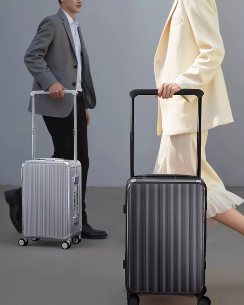 Two people with suitcases, one silver and one black, on a gray background